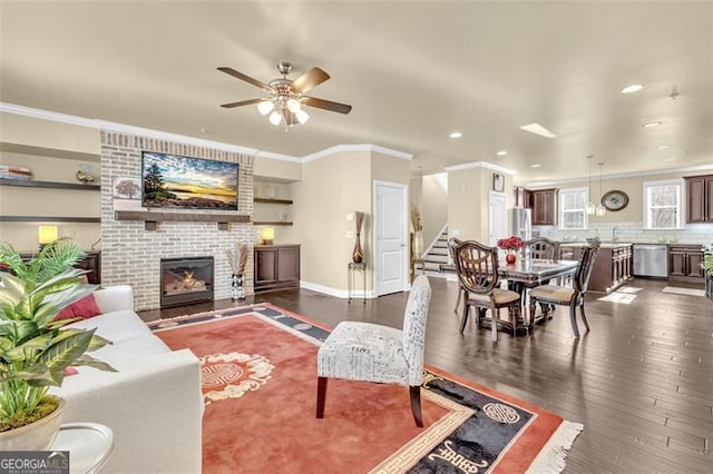 living area with dark wood-style floors, stairs, crown molding, a brick fireplace, and recessed lighting