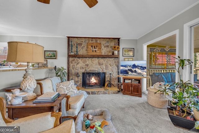 carpeted living room with ceiling fan, a stone fireplace, and crown molding