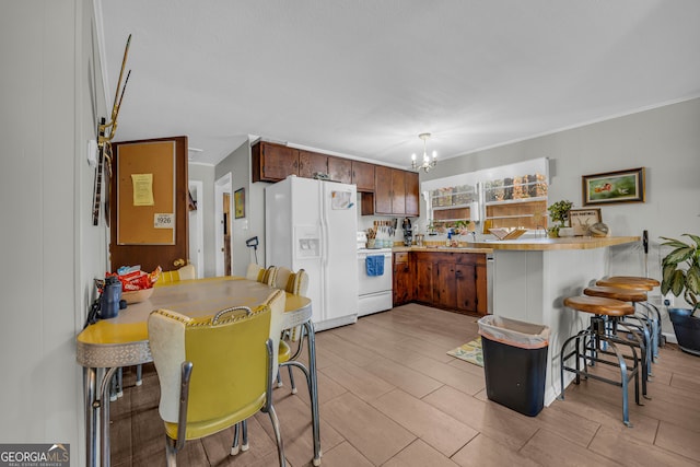 kitchen featuring white appliances, decorative light fixtures, kitchen peninsula, a breakfast bar area, and a chandelier