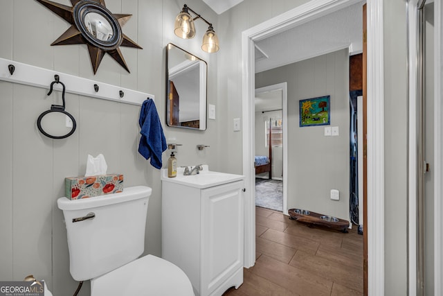 bathroom featuring wood walls, vanity, wood-type flooring, and toilet