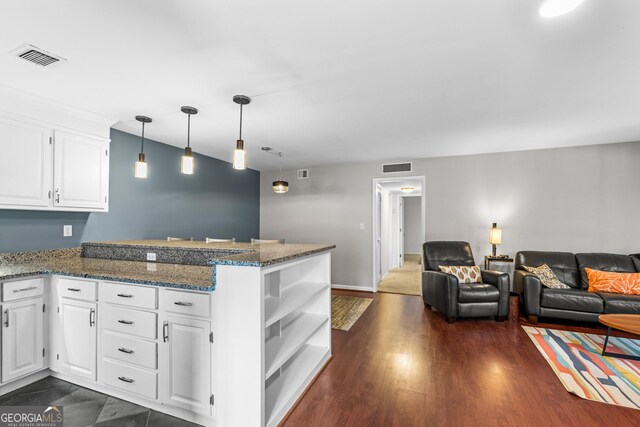 kitchen with kitchen peninsula, dark stone counters, pendant lighting, dark hardwood / wood-style floors, and white cabinetry