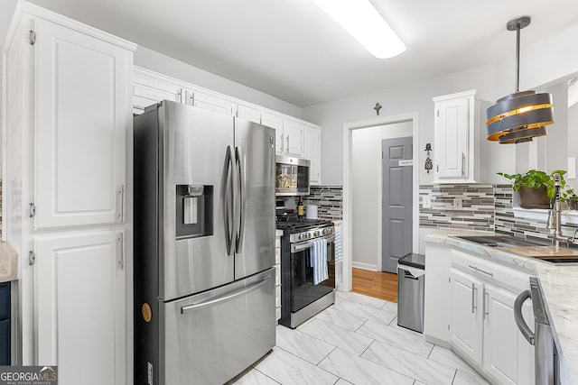 kitchen with decorative backsplash, white cabinets, hanging light fixtures, and appliances with stainless steel finishes