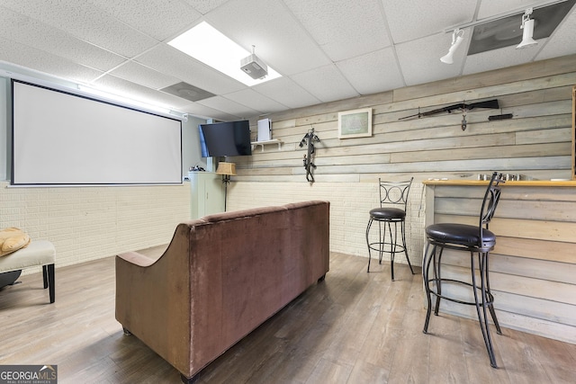 cinema room with a paneled ceiling, wood walls, wood-type flooring, and brick wall