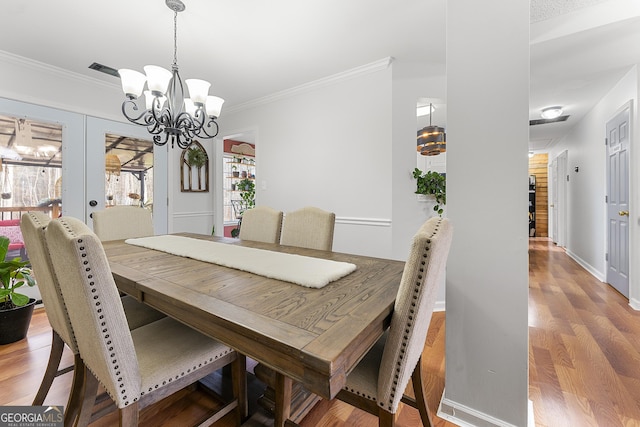 dining area featuring hardwood / wood-style floors, a notable chandelier, crown molding, and french doors