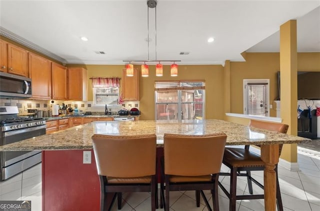 kitchen featuring light tile patterned flooring, hanging light fixtures, appliances with stainless steel finishes, a kitchen island, and a kitchen bar