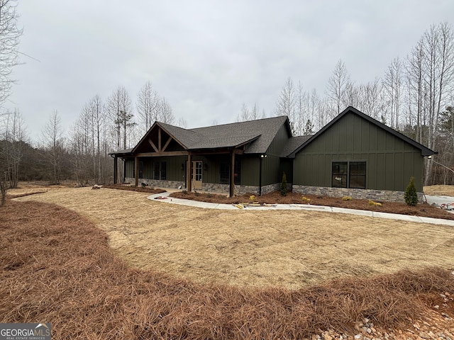 view of front of property featuring stone siding, covered porch, board and batten siding, and roof with shingles