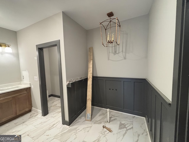 bathroom with marble finish floor, a notable chandelier, a decorative wall, wainscoting, and vanity