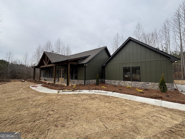 view of front of house with stone siding, a shingled roof, and board and batten siding