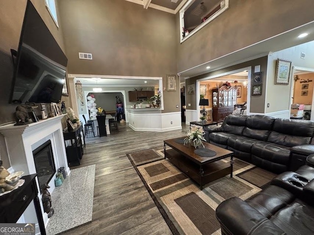 living area featuring a towering ceiling, dark wood-style floors, a premium fireplace, and visible vents