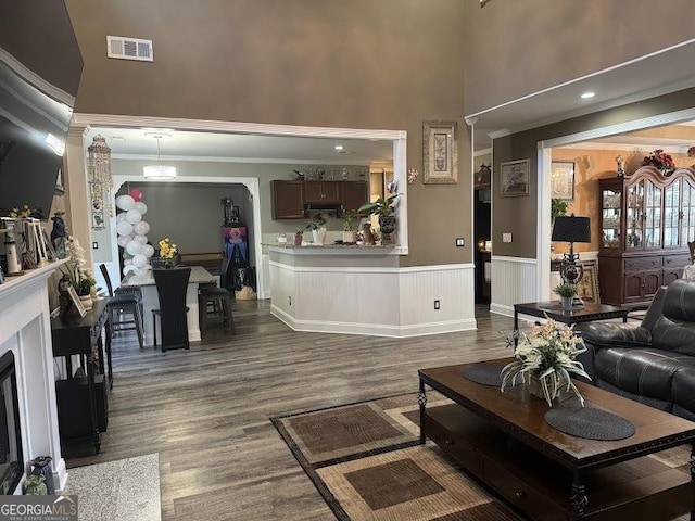 living room with visible vents, wainscoting, a premium fireplace, ornamental molding, and dark wood-type flooring