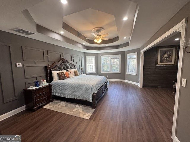 bedroom with dark hardwood / wood-style floors, ceiling fan, and a tray ceiling