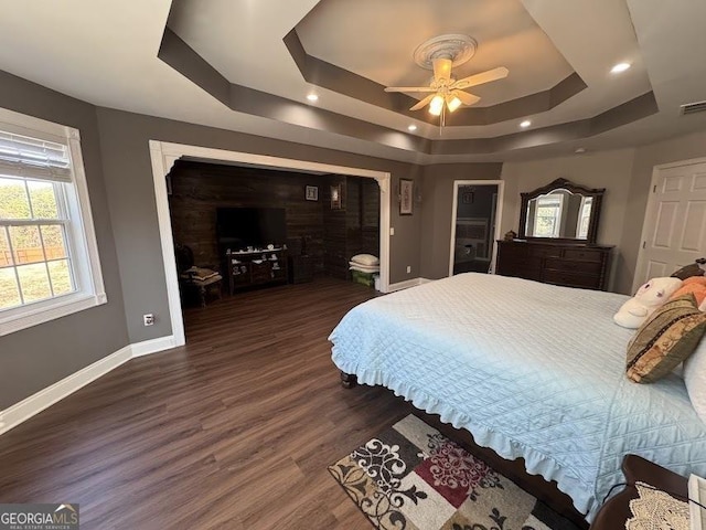 bedroom with a tray ceiling, ceiling fan, and dark wood-type flooring