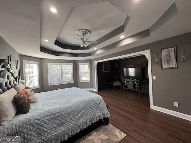 bedroom with a raised ceiling, multiple windows, ceiling fan, and dark hardwood / wood-style flooring