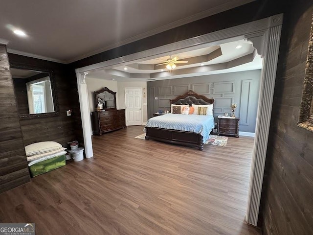 bedroom featuring recessed lighting, wood finished floors, baseboards, a raised ceiling, and crown molding