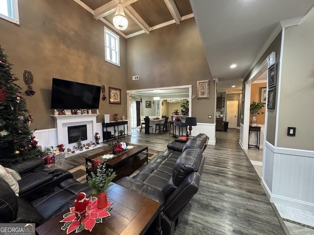 living room with hardwood / wood-style floors, beamed ceiling, a high ceiling, and ornamental molding