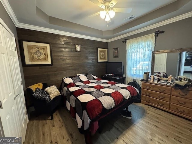 bedroom with a tray ceiling, visible vents, crown molding, and wood finished floors