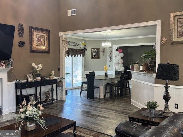 living area with a wainscoted wall, ornamental molding, wood finished floors, and visible vents