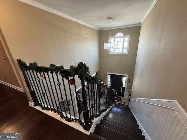 stairway with a chandelier, wood-type flooring, and ornamental molding