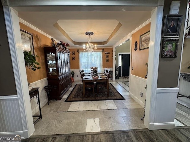 dining room with a wainscoted wall, a tray ceiling, a chandelier, and crown molding