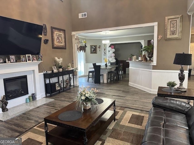 living area with a wainscoted wall, wood finished floors, visible vents, ornamental molding, and a glass covered fireplace