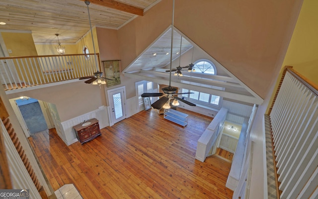 living room with beamed ceiling, ceiling fan with notable chandelier, wood-type flooring, and a high ceiling