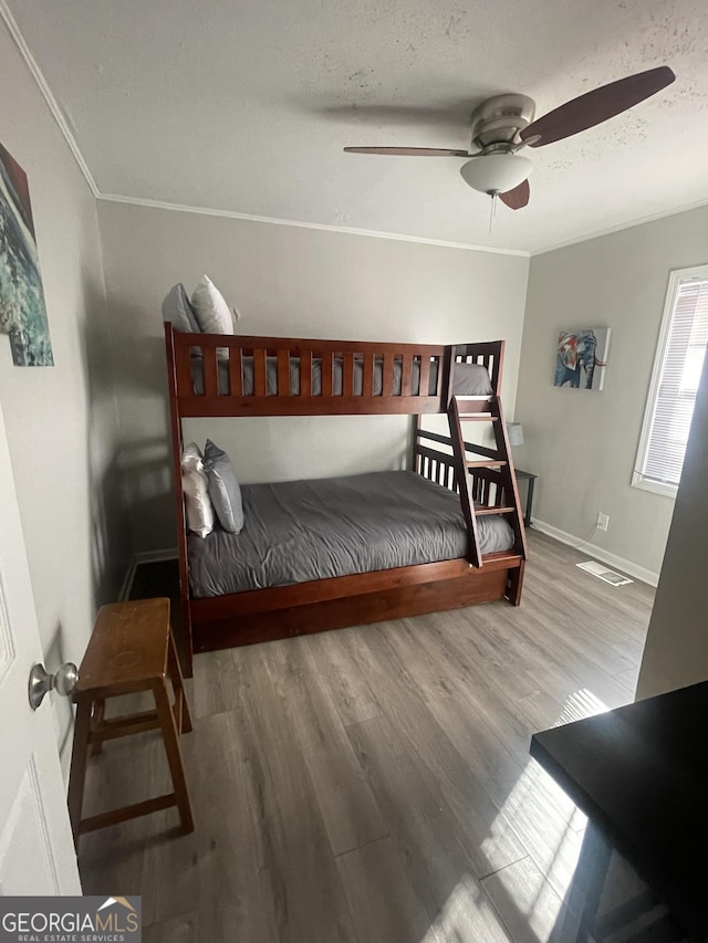 bedroom with a textured ceiling, ceiling fan, wood-type flooring, and crown molding