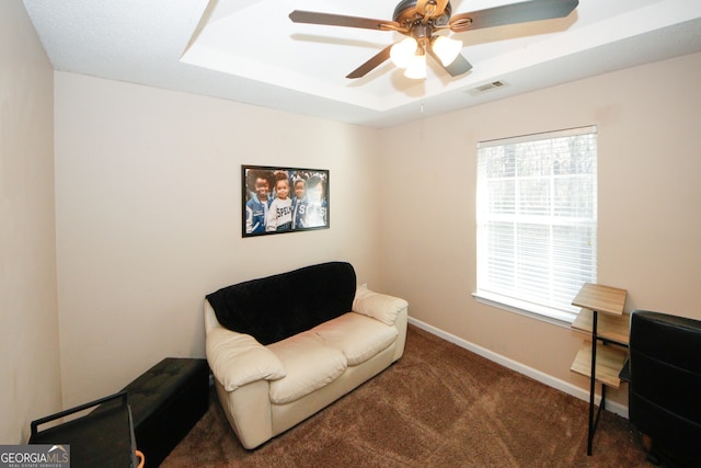 living area with dark colored carpet, a tray ceiling, and ceiling fan