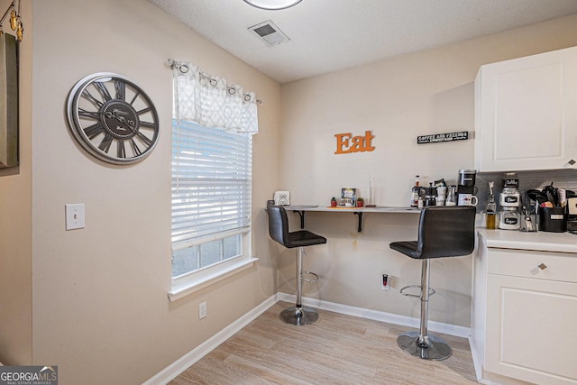 bar with tasteful backsplash, white cabinets, and light hardwood / wood-style floors