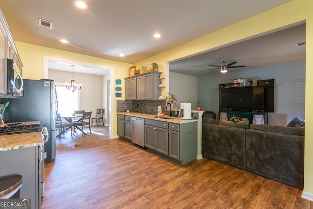 kitchen with pendant lighting, ceiling fan with notable chandelier, sink, dark hardwood / wood-style flooring, and stainless steel appliances