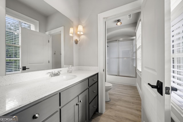 full bathroom with hardwood / wood-style floors, vanity, toilet, and bath / shower combo with glass door