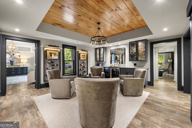 living room featuring a raised ceiling, a notable chandelier, wood-type flooring, indoor bar, and wood ceiling