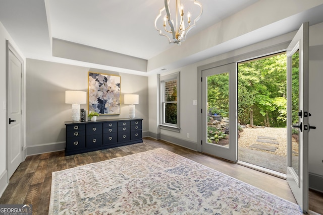 doorway featuring a tray ceiling, an inviting chandelier, and dark wood-type flooring