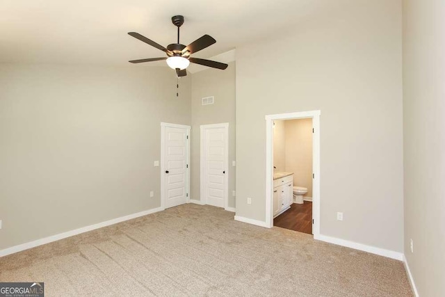 unfurnished bedroom with dark colored carpet, a towering ceiling, ensuite bath, and ceiling fan