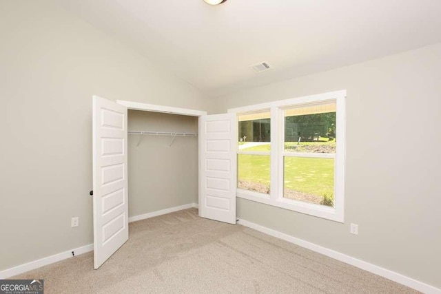 unfurnished bedroom featuring light carpet, a closet, and lofted ceiling