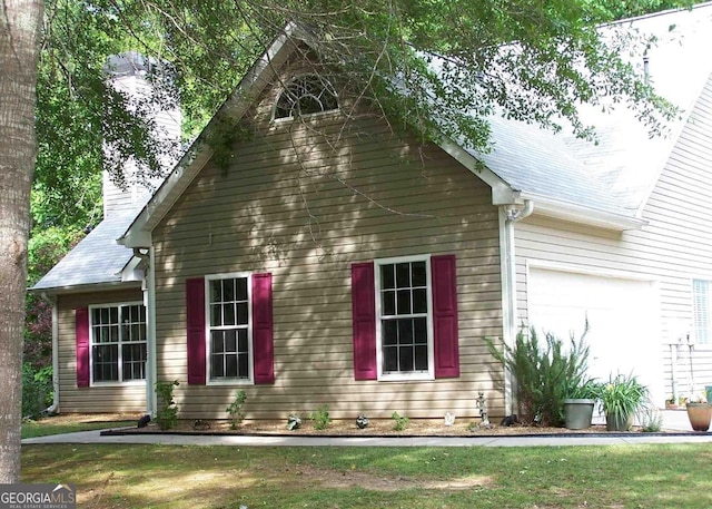 view of side of property featuring a garage, a shingled roof, and a yard