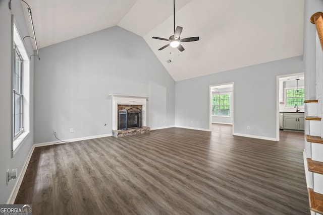unfurnished living room with dark wood finished floors, ceiling fan, a fireplace, baseboards, and high vaulted ceiling