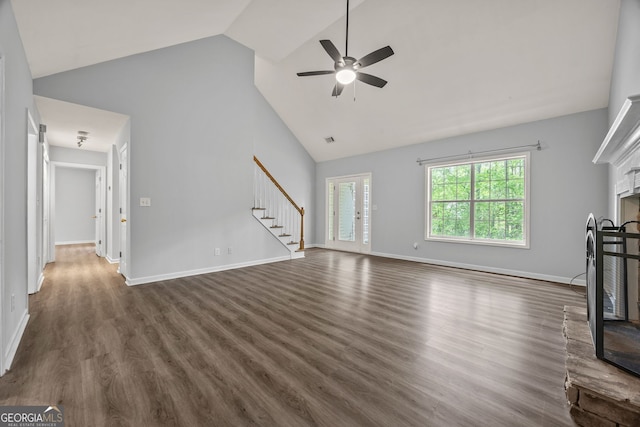 unfurnished living room featuring ceiling fan, a fireplace with raised hearth, dark wood finished floors, high vaulted ceiling, and stairs