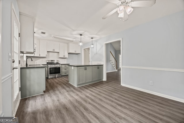 kitchen with a sink, ceiling fan, dark countertops, stainless steel gas range oven, and wood finished floors
