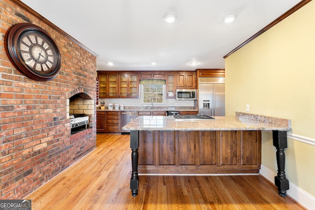 kitchen featuring kitchen peninsula, a kitchen breakfast bar, light wood-type flooring, light stone counters, and stainless steel appliances