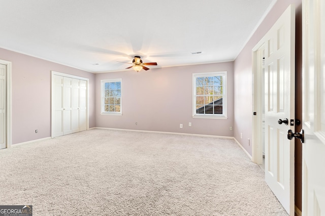 unfurnished bedroom featuring multiple closets, ceiling fan, and light carpet