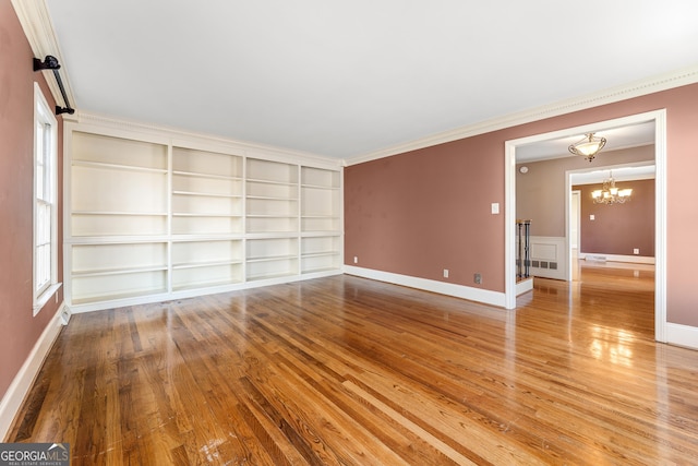 spare room featuring built in shelves, ornamental molding, a chandelier, and hardwood / wood-style flooring