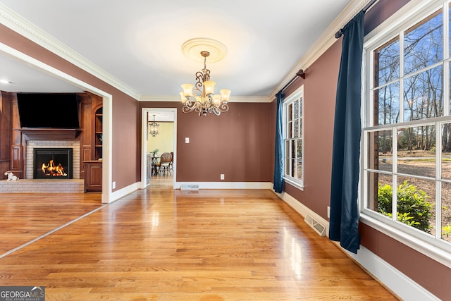 unfurnished dining area featuring a fireplace, ornamental molding, light hardwood / wood-style floors, and a notable chandelier