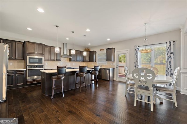 kitchen featuring a center island, wall chimney exhaust hood, dark hardwood / wood-style floors, decorative light fixtures, and stainless steel appliances