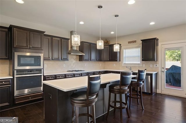 kitchen with a kitchen breakfast bar, stainless steel appliances, dark hardwood / wood-style floors, a kitchen island, and hanging light fixtures