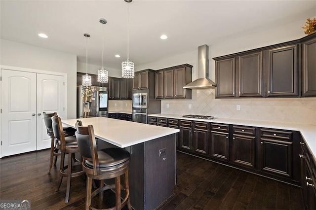 kitchen featuring wall chimney exhaust hood, hanging light fixtures, dark hardwood / wood-style floors, a kitchen island, and appliances with stainless steel finishes