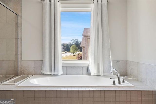 bathroom with tiled tub and a healthy amount of sunlight