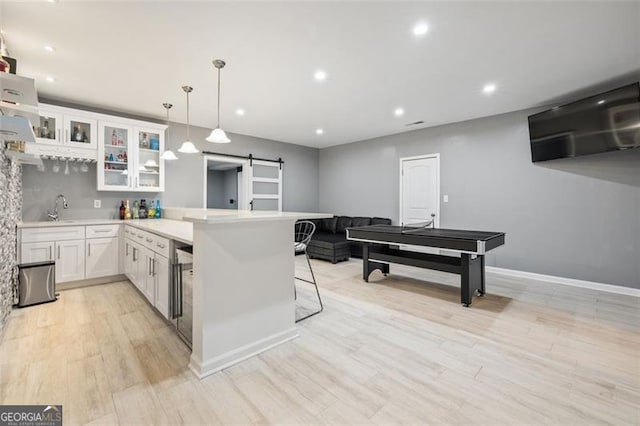 kitchen with kitchen peninsula, a kitchen bar, a barn door, white cabinetry, and hanging light fixtures