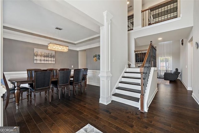 dining room with ornate columns, crown molding, dark wood-type flooring, and a notable chandelier