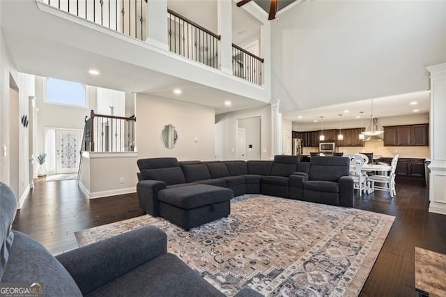 living room featuring decorative columns, ceiling fan, dark wood-type flooring, and a high ceiling