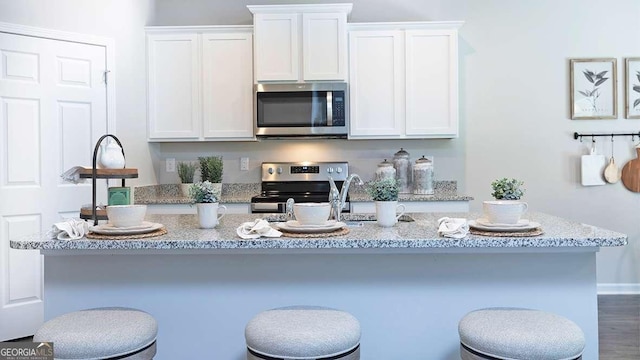 kitchen with a kitchen bar, appliances with stainless steel finishes, white cabinets, dark hardwood / wood-style floors, and an island with sink